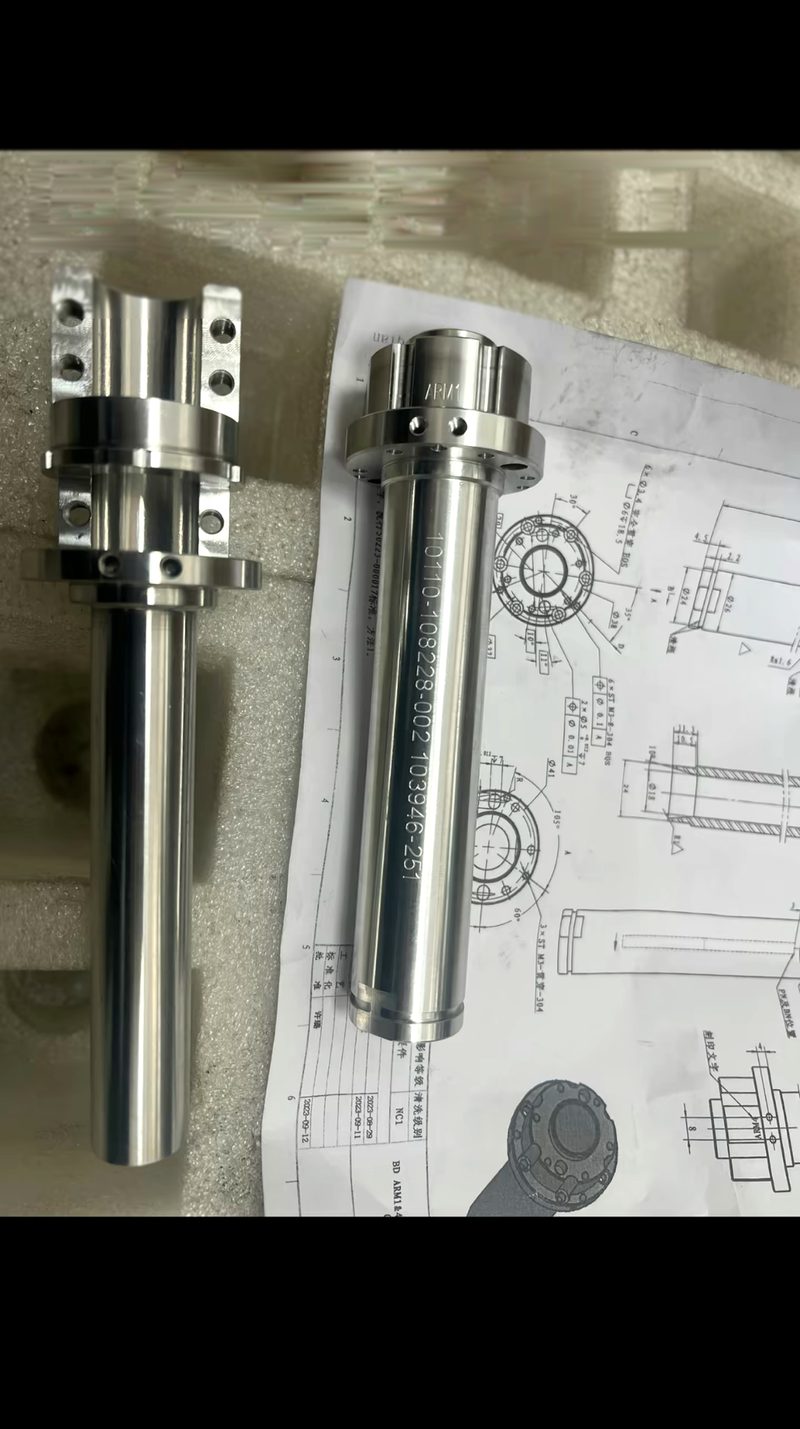 Two precision machined stainless shaft components laid on their engineering drawings before packing